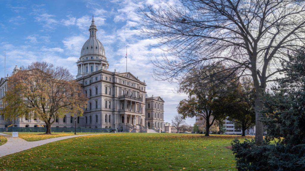 Michigan's capitol building surrounded by trees and a lawn with fallen leaves.